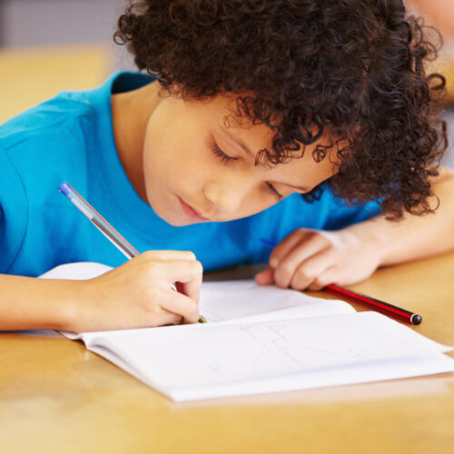 Boy, writing and book in school classroom for learning, focus or development for future. Male child, pen and paper for studying, education and test for thinking, scholarship or concentration in class.